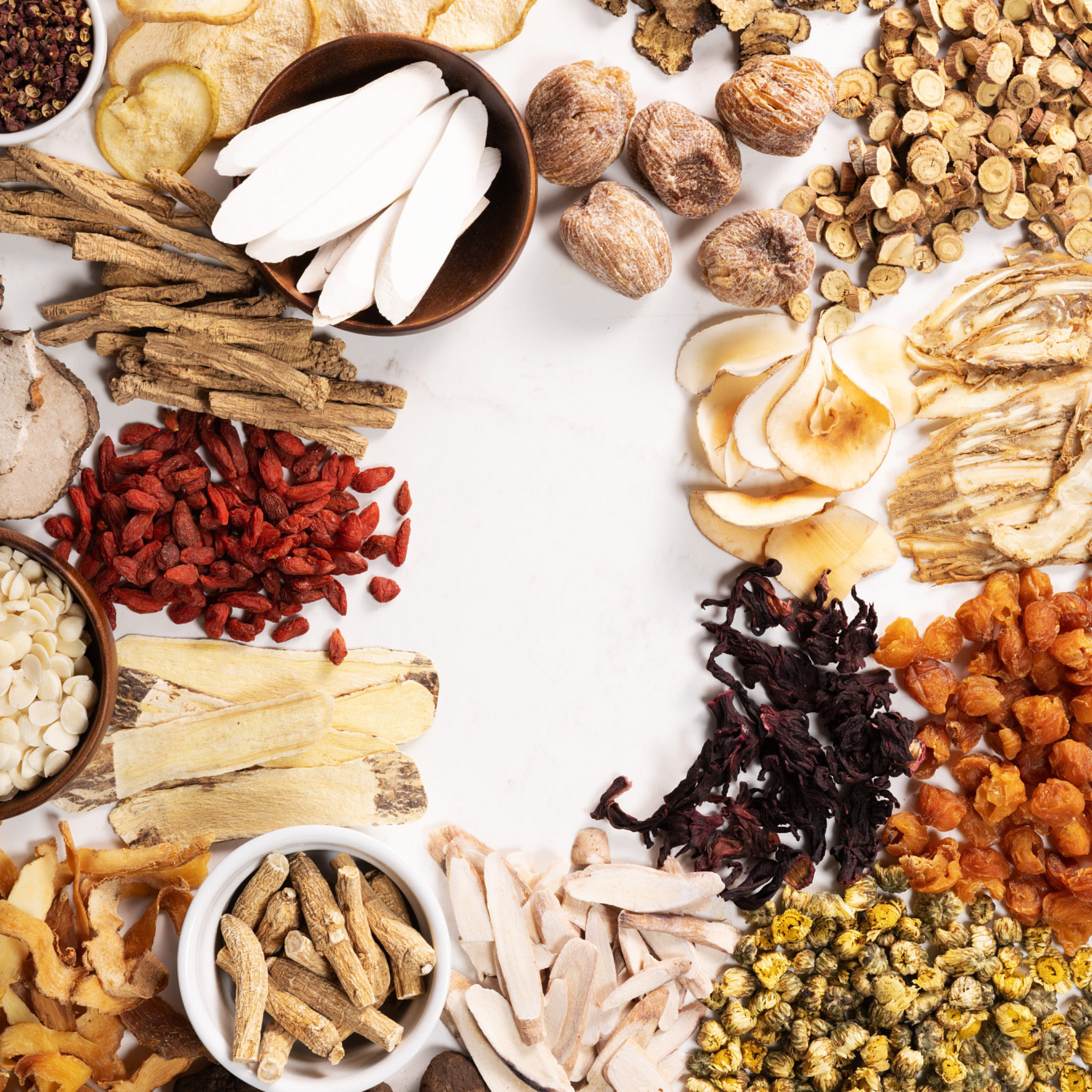 An overhead flat-lay arrangement of various dried and fresh herbal ingredients arranged around a white central background.