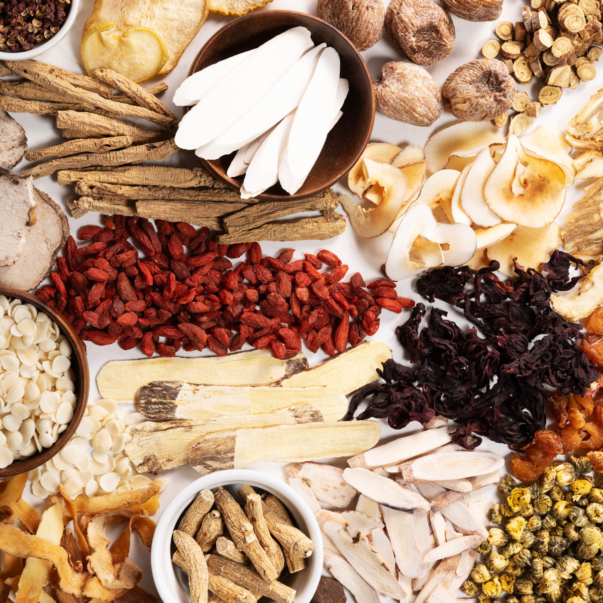 An overhead flat-lay arrangement of various dried and fresh herbal ingredients arranged around a white central background.
