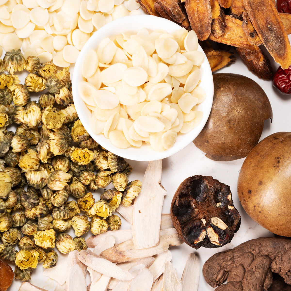 A top-down flat lay of dried herbal ingredients including Siraita, South and North Almonds, Processed Black Ginger,  Candied Licorice, Baby Chrysanthemum