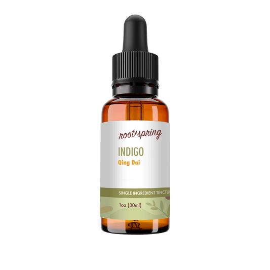 A 1 oz amber glass dropper bottle of Root+Spring Tincture of the Month, Indigo, with a white label and black dropper cap, isolated on a white background.