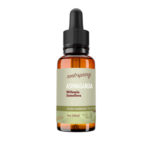 A 1 oz amber glass dropper bottle of Root+Spring Ashwaganda tincture with a black dropper cap and a light olive-green label, shown on a transparent background.